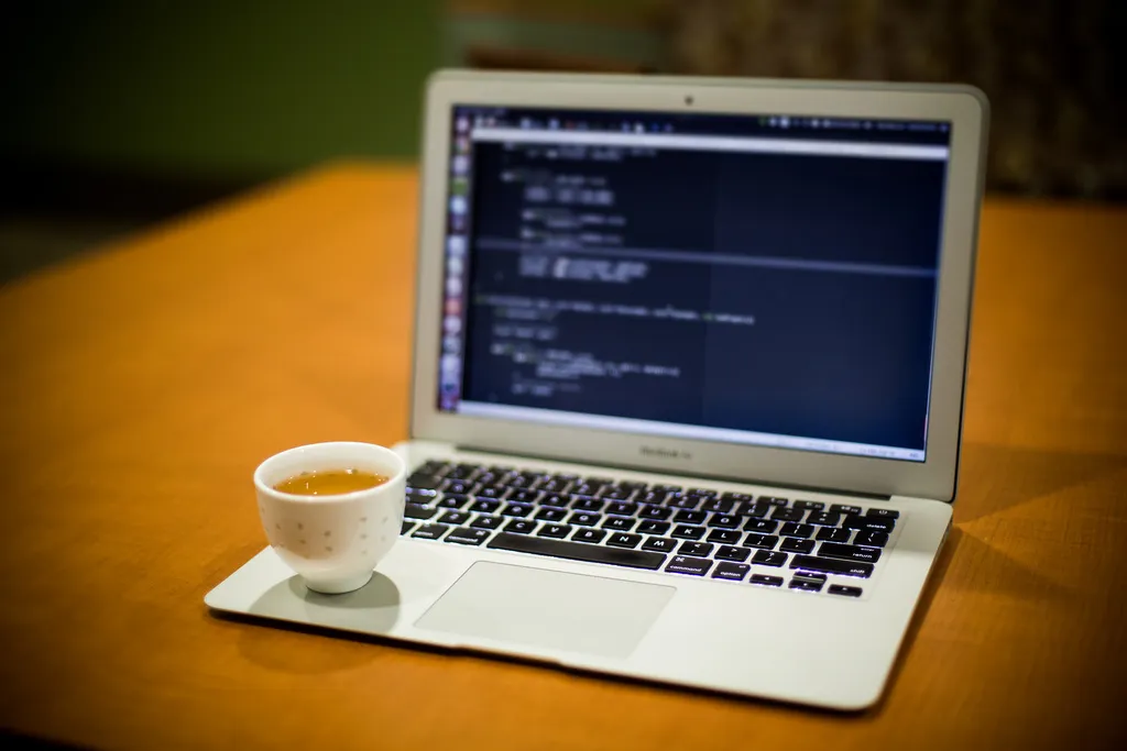 Laptop with code on screen next to a cup of tea